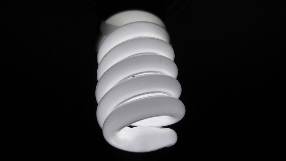 Detailed view of a spiral fluorescent light bulb on a black background.